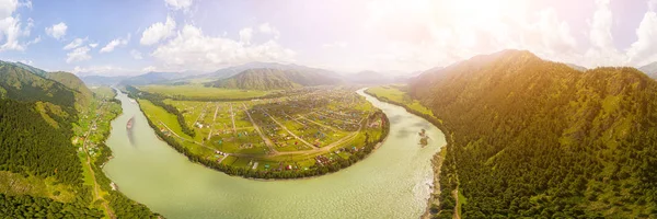 Panoramic view on mountain river, small village in front of mountain range.  National park in Altai republic. Aerial wide angle drone view of  river