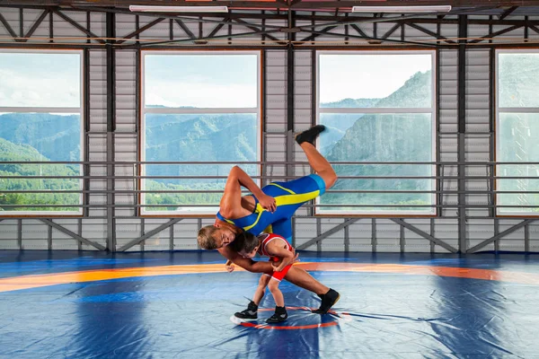 The little boy in sport tights wrestler throws over the hip adult male wrestler on a wrestling carpet in the gym. The concept of child power and martial arts training. Teaching children Greco-Roman wrestling