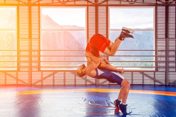 The concept of fair wrestling. Two greco-roman  wrestlers in sportwears makes a throw through the chest  on a wrestling carpet in the gym.The concept of male wrestling and resistance