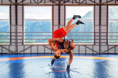 Greko-Romen güreş eğitimi, boğuşma. Kırmızı ve mavi üniformalı iki greko-romen güreşçi spor salonunda güreş halısında uyluk atışı yapıyor. Erkek güreşve direnç kavramı