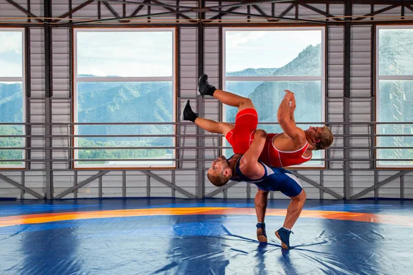 Two men in sports wrestling tights and wrestling during a traditional Greco-Roman wrestling in fight on a wrestling mat against the backdrop of mountains. Wrestler throws his opponents chest through