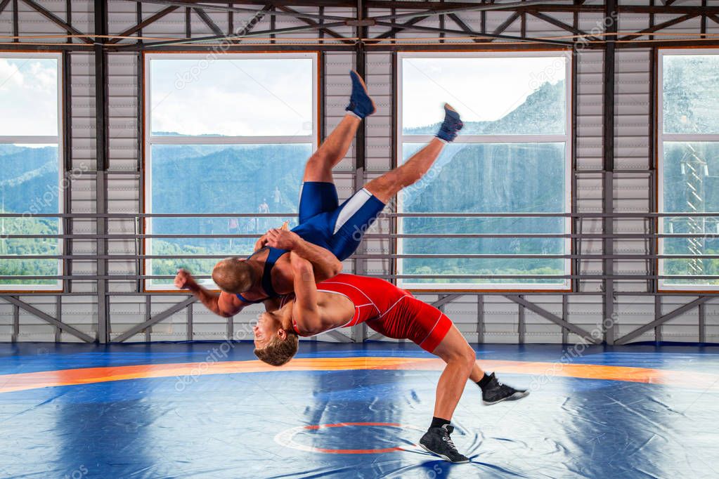 Two men in sports wrestling tights and wrestling during a traditional Greco-Roman wrestling in fight on a wrestling mat against the backdrop of mountains. Wrestler throws his opponents chest through 