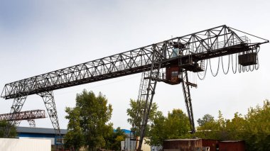 bir şantiyede büyük metal gantry vinç, mal depolamak için arka planda endüstriyel depolarda. Mavi gökyüzüne karşı gantry vinç rulman metal yapıları türü