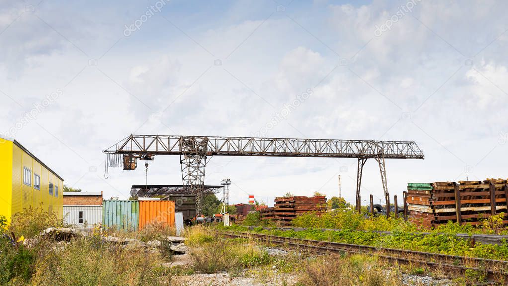large metal gantry crane at a construction site, in the background industrial warehouses for storing goods. Type of bearing metal structures of gantry crane against the blue sky