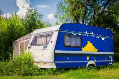 Kosova'nın ulusal bayrağına boyanmış bir araba römorku, bir motorlu ev, dağlık bir alanda park halinde duruyor. Ülkeler arasında karayolu taşımacılığı, ticareti, ihracatı ve ithalatı kavramı.