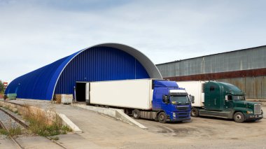 Teslim ve tedarik konsept görüntü. Yükleme alanındaki tesiste kamyonlar yükleniyor. Malların depolanması için büyük bir metal sanayi deposu . 