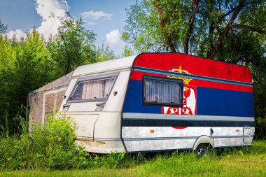 Sırbistan'ın ulusal bayrağına boyanmış bir araba römorku, bir motorlu ev, dağlık bir alanda park halinde duruyor. Ülkeler arasında karayolu taşımacılığı, ticareti, ihracatı ve ithalatı kavramı.