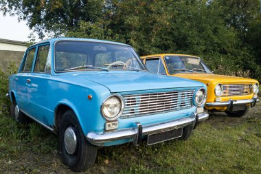 Yuvarlak farlar ile iki parlak mavi ve sarı retromachines ormanın arka plan karşı yeşil çim üzerinde durmak. Yirmili yaşların ortasında yaşlı manikürlü araba kavramı