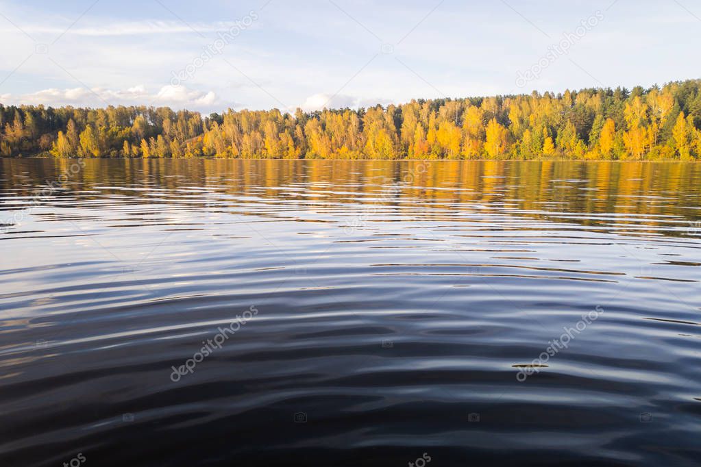 Beautiful landscape from the water. The water surface of the lake, followed by yellow autumn and bright sunshine. Beautiful autumn landscape