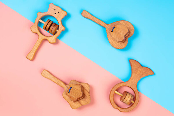 Многоцветная квартира лежала с экологически чистыми деревянными игрушками, гремит в виде сердца, рыбы, звезд, медведя на розовом и голубом изолированном фоне. Вид сверху, соблазн для обучения и развлечений детей
 