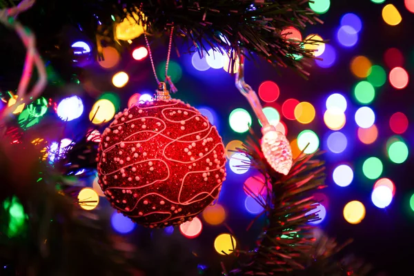 背景にクリスマスツリーにぶら下がっている赤い光沢のあるクリスマスボールのクローズアップは さまざまな色で輝く多くのガーランド 新年とクリスマスのコンセプト 美しく装飾されたクリスマスツリー — ストック写真