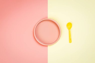 Minimalist düz ağaç kabuğu, pembe plastik bir plaka ve sarı-pembe izole bir arka planda sarı bir kaşık. Mesajın için plastik sofra takımı, Moup. Çocuk oyunları için tabaklar 