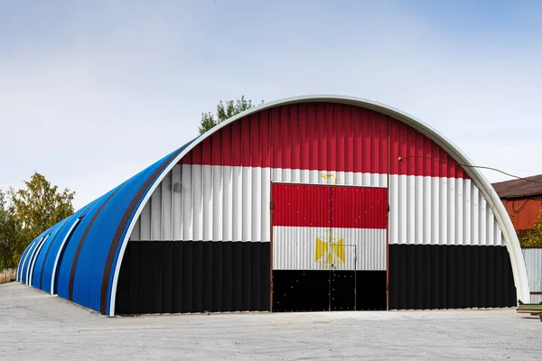 Close-up of the national flag of Egypt painted on the metal wall of a large warehouse the closed territory against blue sky. The concept of storage of goods, entry to a closed area, logistics