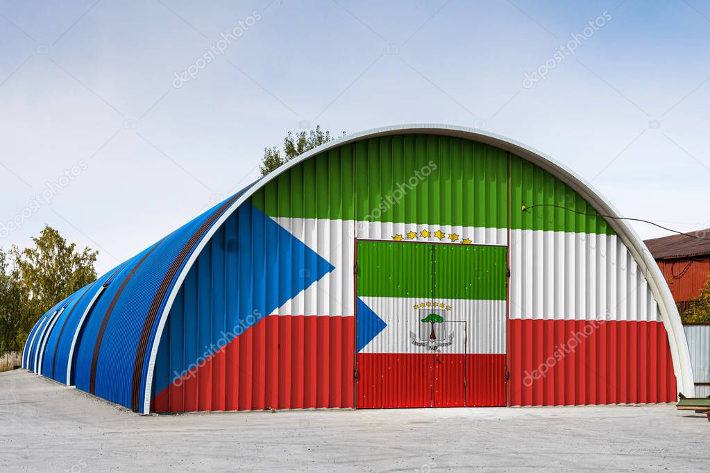 Close-up of the national flag of Equatorial Guinea painted on the metal wall of a large warehouse the closed territory against blue sky. The concept of storage of goods, entry to a closed area, logistics