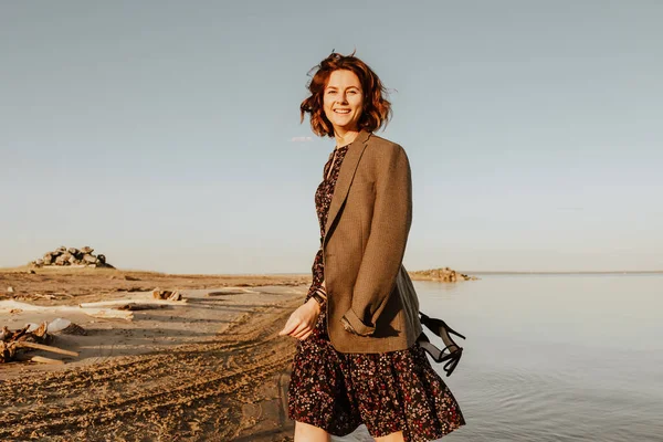 Posing woman in nature. Young woman in stylish clothes: dark dress and jacket posing against the backdrop of a  sea. Photos on vacation in the fall