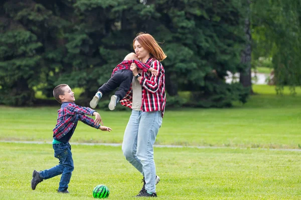 幸せな若い母親は緑の芝生の公園で赤ちゃんと一緒にボールで遊んでいます 幸せな家族の概念 母の日 — ストック写真