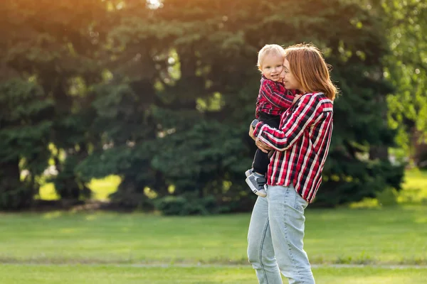 幸せな若い母親は緑の芝生の公園で彼女の赤ちゃんと遊んでいます 幸せな家族の概念 母の日 母と息子は休暇で一緒に活動しています — ストック写真