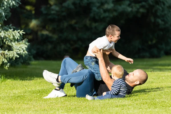 Happy young daddy is playing with  her baby in a park on a green lawn.Concept of a happy family. Fathers Day. Dad and son have activities together on holidays.