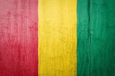 Ulusal Gine bayrağı eski tekstil üzerinde boya renkleriyle tasvir ediliyor. Kumaş dokusu arka planında bayrak pankartı.