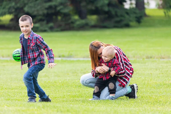 幸せな若い母親は緑の芝生の公園で赤ちゃんと一緒にボールで遊んでいます 幸せな家族の概念 母の日 — ストック写真