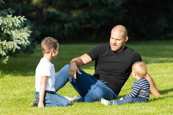 幸せな若いお父さんは緑の芝生の公園で彼女の赤ちゃんと息子と遊んでいます 幸せな家族の概念 父の日 パパと息子は休暇で一緒に活動してる — ストック写真