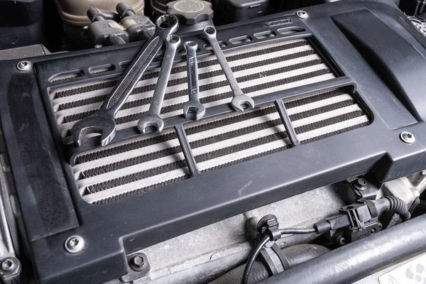 A set of metal spanners of different sizes lies under the hood of the car on an oil cooler. Concept of car repair and tools in car service