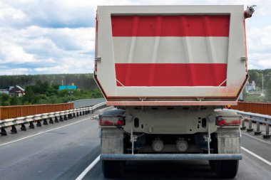 Avusturya bayrağı taşıyan büyük bir kamyon, köy ve orman manzarasının arka planına karşı otoyolda ilerliyor. İhracat-ithalat, ulaşım, malların ulusal teslimatı 