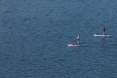 Novosibirsk / Rusya 27 Haziran 2020: Kürekleri olan iki kadın sporcu güneşli bir günde nehir boyunca sörf tahtalarında yüzüyor. Paddleboard 