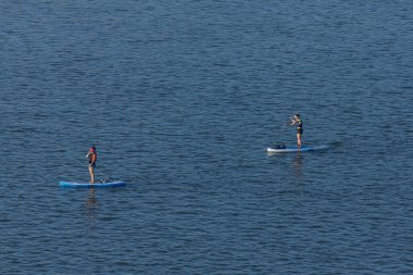 Novosibirsk / Rusya 27 Haziran 2020: Kürekleri olan iki kadın sporcu güneşli bir günde nehir boyunca sörf tahtalarında yüzüyor. Paddleboard 
