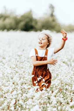 Küçük kız koşar, güneşli bir yaz gününde buğday tarlasında günün tadını çıkarır..
