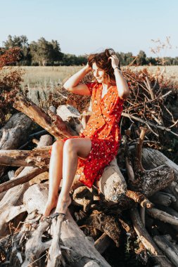 Kırmızı elbiseli, gülen, yaşlı kütüklere poz veren modaya uygun genç bir kadının moda portresi.