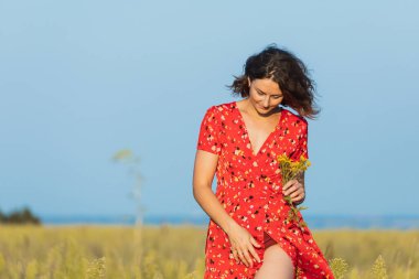 Güneşli bir sonbahar gününde arka planda güzel, genç ve kırmızı elbiseli bir mankenin portresi. Kadınların ve doğanın birliği, barışçıl ruh hali, çevre dostu yaşam.