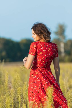Koyu renk saçlı bir kadın gülümsüyor, yaz günü romantik elbiseler içinde yeşil alanda yürüyor. Köyde yaz tatili ve yaşam tarzı kavramı