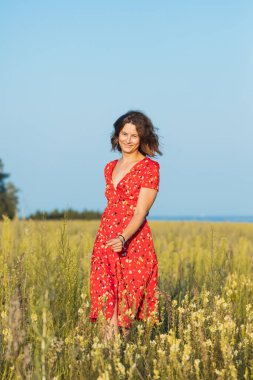 Koyu renk saçlı bir kadın gülümsüyor, yaz günü romantik elbiseler içinde yeşil alanda yürüyor. Köyde yaz tatili ve yaşam tarzı kavramı