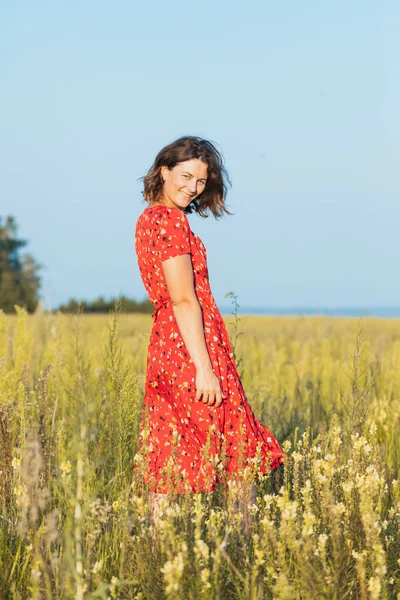 Güzel elbiseli güzel bir kadın gün batımında çayırda gülüyor ve dans ediyor. Livestyle yürüyüş konsepti