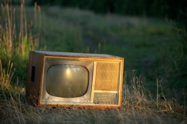 Batan güneş ışınlarının altında bir buğday arka planına karşı tarla yolunda eski bir retro TV seti