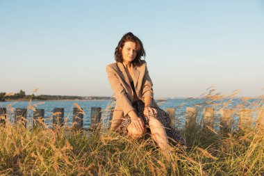 Bej ceketli ve etekli güzel bir mankenin portresi güneşli bir sonbahar gününde arka planda günün tadını çıkar. Kadınların ve doğanın birliği, barışçıl ruh hali, çevre dostu yaşam.