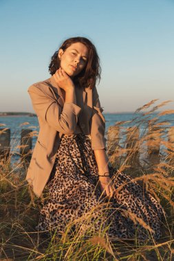 Sıcak giysiler içinde güzel bir genç modelin portresi güneşli bir sonbahar gününde arka planda günün tadını çıkarır. Sonbahar sıcacık fotoğrafı. Gülümseyen ve yüzünü çeviren, neşeli bir kadın..