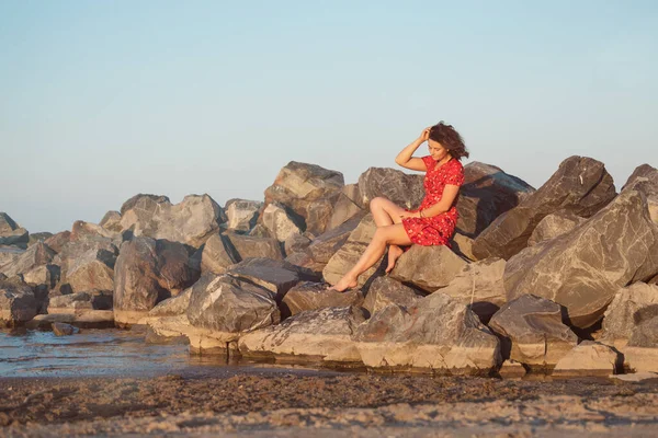 Romantyczny Spacer Kręconej Kobiety Czerwonej Sukience Pozującej Kamieniu Morzu Koncepcja — Zdjęcie stockowe