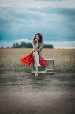 Kıvırcık saçlı, kırmızı elbiseli ve paltolu bir kadının eski bir retro TV 'de arka planda oturduğu romantik bir yürüyüş. Kadın özgürlüğü, özgürlük ve aşk kavramı.