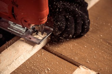 İş kıyafetleri içinde deneyimli bir marangoz ve küçük büstiyer sahibi marangoz, hafif bir atölyede bir testereyle ahşap bir barın kenarlarını gördü ve işledi. 