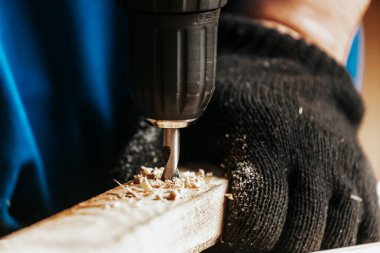 Ev onarım konseptleri, yakın çekim. Marangozluk. Dolap yapımcısı elleri atölyedeki çalışma masasındaki tornavidayı kullanarak tahta bir tahta deliyor.