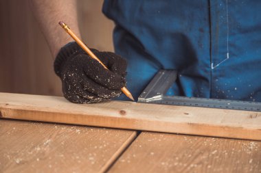 Adamın eli ahşap bir tahtaya bir kalem ve bir ölçü cetveli ile işaret koyuyor.. 