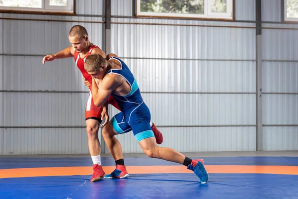 ギリシャ ローマのレスリングのトレーニング グラップリング 赤と青のユニフォームを着た2人のグレコ ローマの力士が体操のレスリングカーペットでレスリングをしています — ストック写真