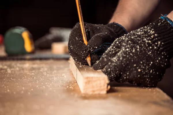 CLose up of the carpenter with a pencil and tape measure mark on wooden board on table. Construction industry, housework do it yoursel. Work with wooden