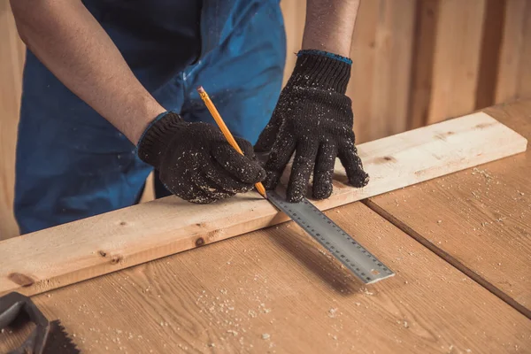 Kalem ve paslanmaz çelik kullanan yakın plan bir adam ahşap bir tahta üzerine dikey bir çizgi çeker..