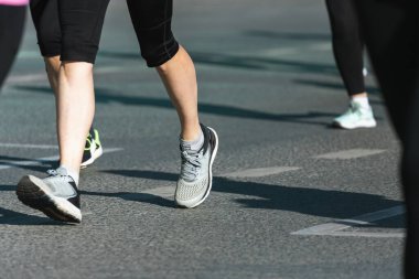 Asfalttaki koşu pisti ve saha atletlerinin bacaklarına yakın çekim. Maraton koşucuları özel spor ayakkabılarla