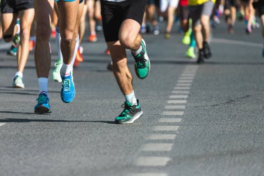 Asfalttaki koşu pisti ve saha atletlerinin bacaklarına yakın çekim. Maraton koşucuları özel spor ayakkabılarla