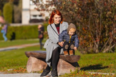 Anne, sıcak bir yaz gününde küçük oğlunun ahşap bir bankta ilk adımlarını atmasına yardım eder. Mutlu çocukluk kavramı