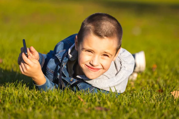 Cheerful Boy Denim Jacket Lies Green Lawn Plays Smartphone City — Stock Photo, Image